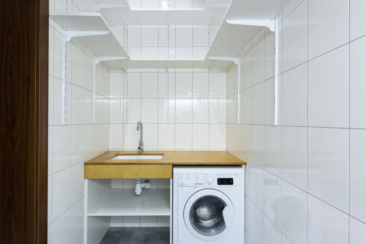 Modern tiled laundry area with a front-loading washing machine and shelves