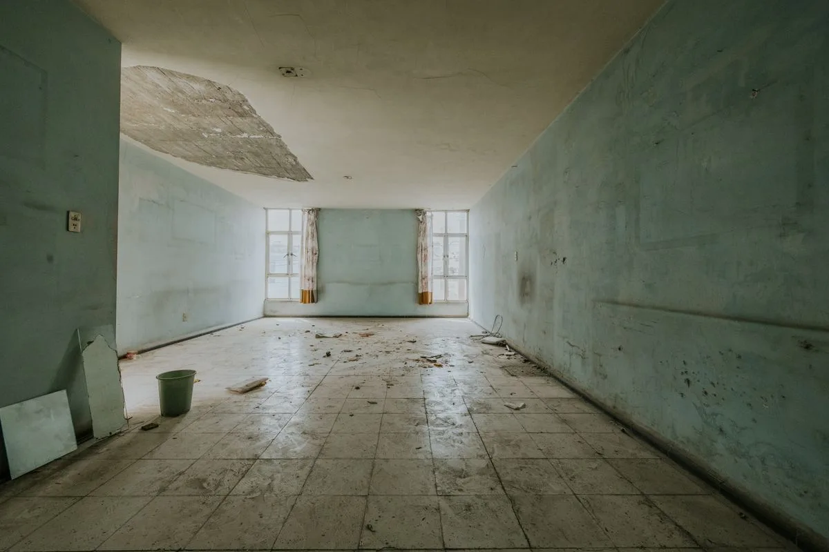 Empty room showing a patched ceiling and water-stained tile floor from a past leak