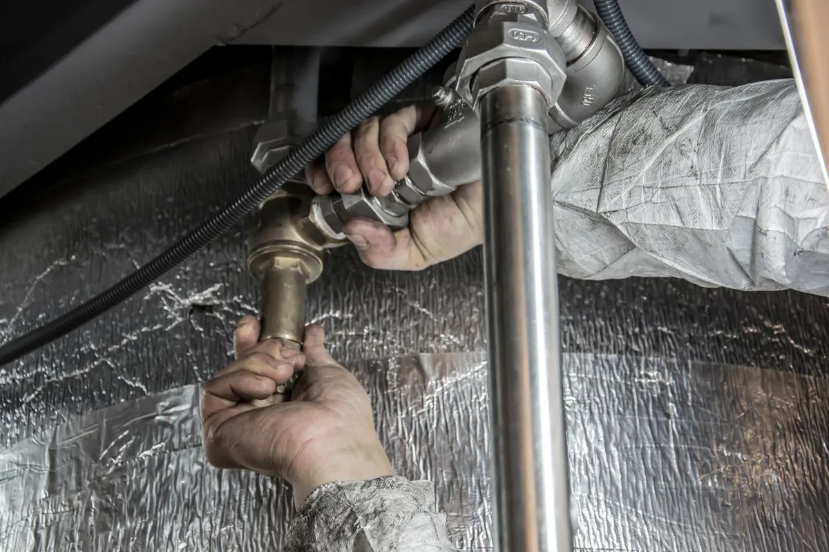 Plumber's hands tightening fittings on steel pipes in a cramped mechanical space