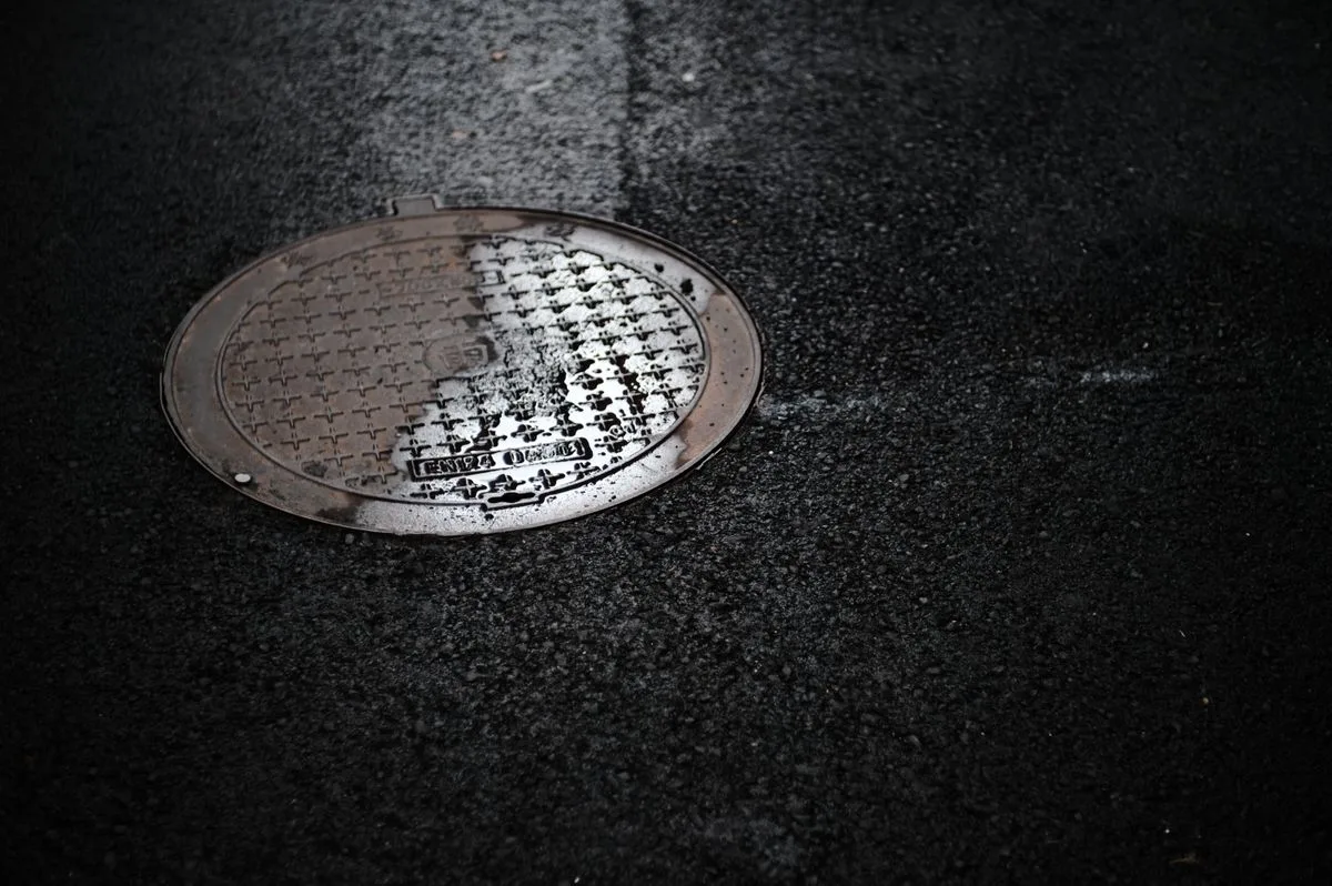Round sewer manhole cover on dark wet asphalt at night
