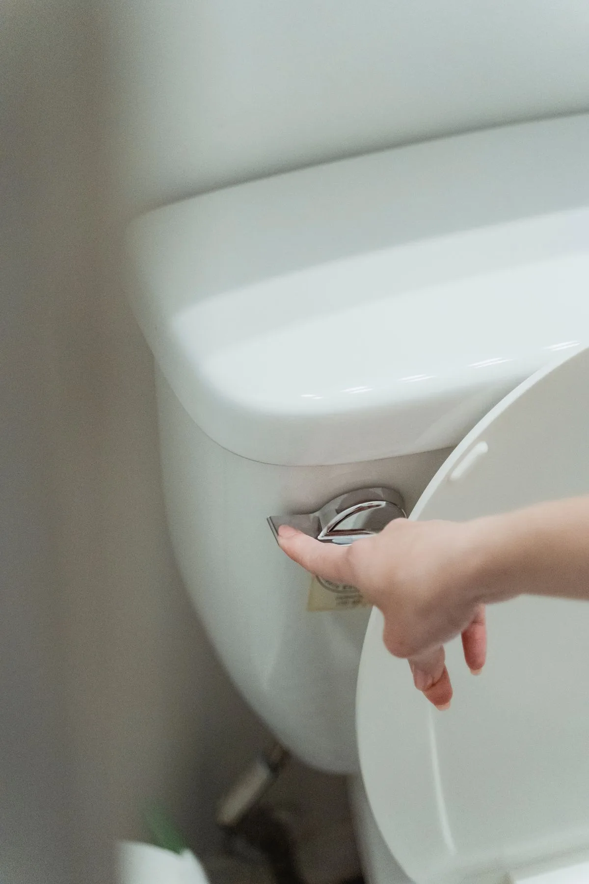 Close-up of a hand pressing the flush handle of a white toilet tank
